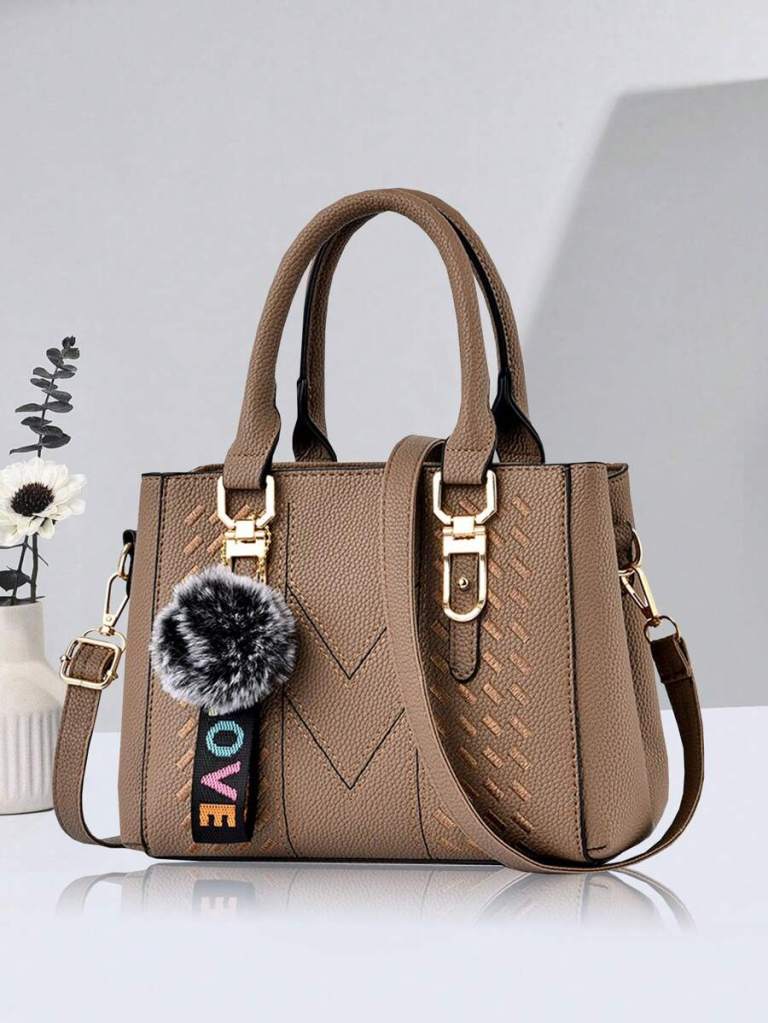 A stylish brown handbag with a textured finish, featuring dual handles and a detachable shoulder strap, adorned with a colorful 'LOVE' tag and a fluffy pom-pom charm.
