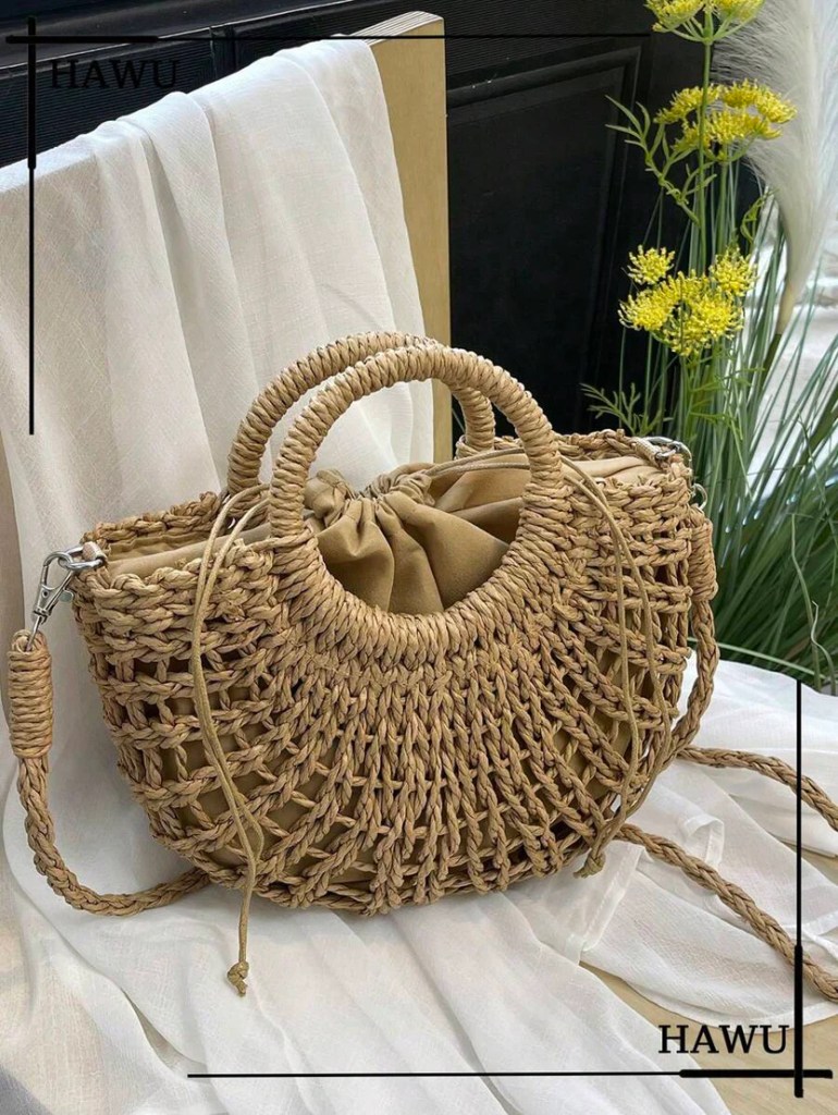 A stylish woven straw handbag with a round handle and a drawstring closure, placed on a soft white fabric backdrop with greenery in the background.