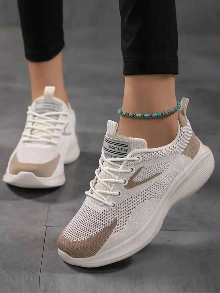 A close-up view of a person's foot wearing white and beige athletic sneakers, showcasing a modern design and breathable material. The leg is adorned with a turquoise beaded anklet.