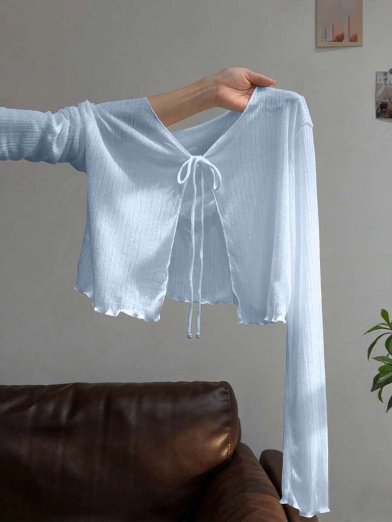 A person holding a light blue, long-sleeved cropped shirt with a V-neck and tie detail in the front.