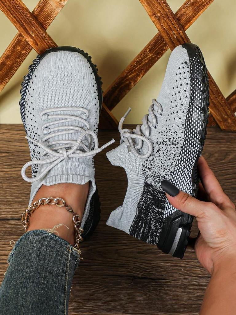 A close-up of a person's foot wearing a gray and black athletic shoe, with a textured design and laces visible, set against a wooden background.